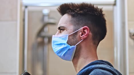 handsome man blow dry his hair in the bathroom wearing protective medical mask