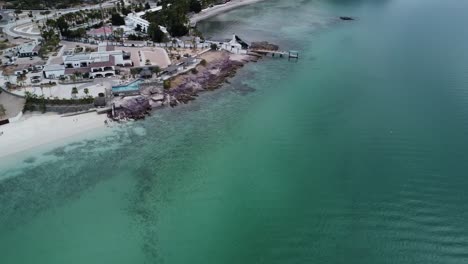 Luftparallaxenaufnahme-über-Der-Wunderschönen-Küste-Von-Playa-El-Caymancito-In-Der-Nähe-Von-La-Paz-Baja-California-Sur-Mexico-Am-Strand-Mit-Hotelgebäuden,-Türkisfarbenem-Meer-Und-Trockener-Sommerlandschaft