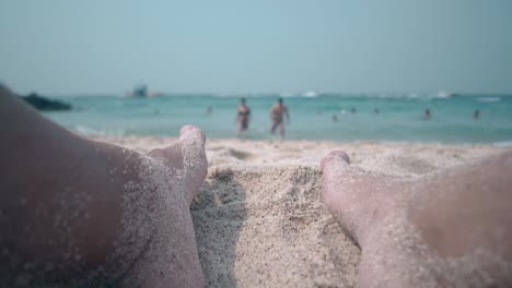 young man feet on sandy beach against blue ocean with people