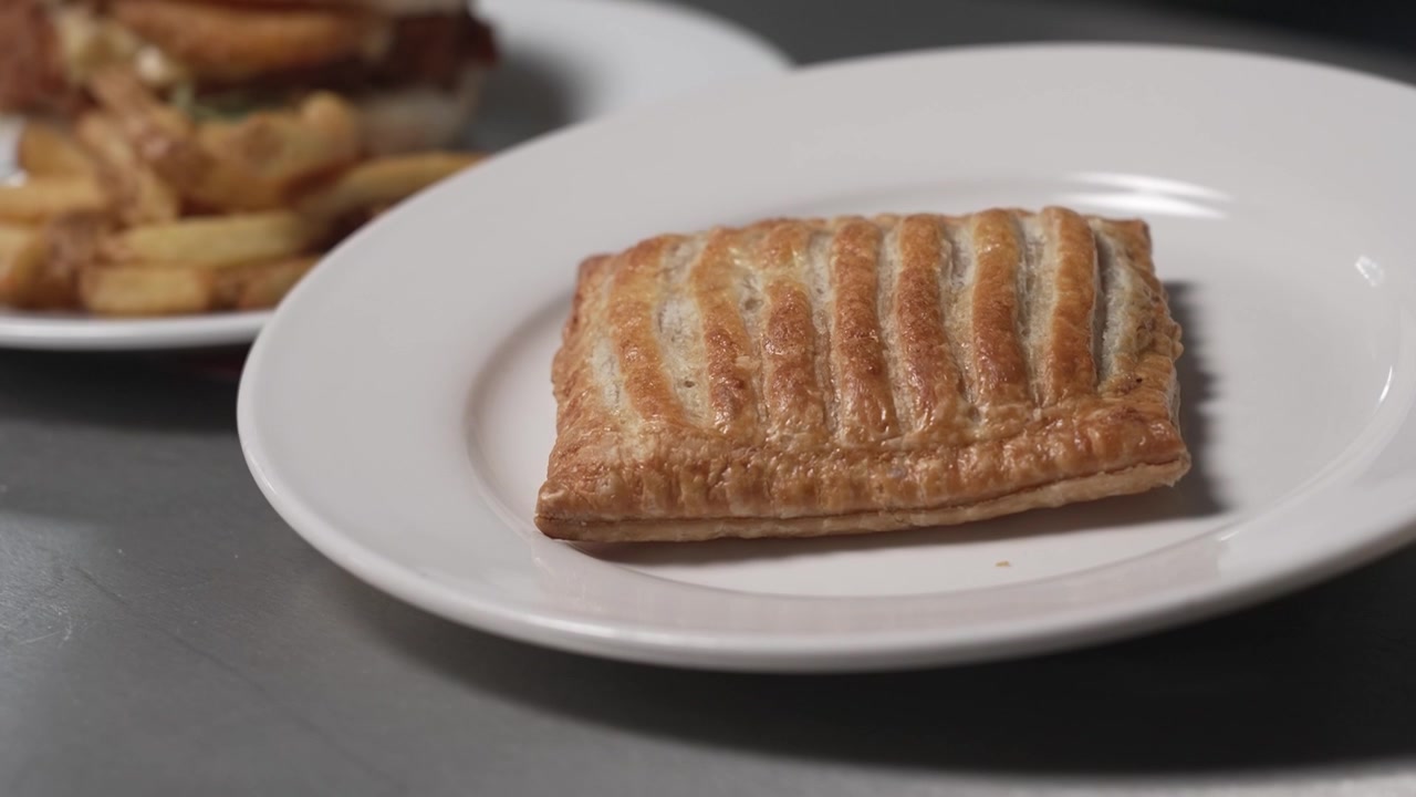 Panoramica verso l'alto su una torta salata ripiena di carne di Greggs, che si trova su un piatto bianco.
