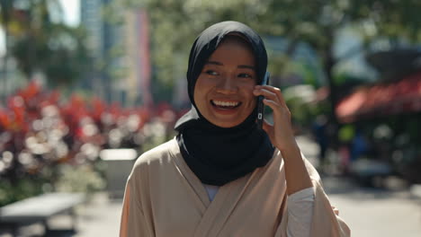 young muslim woman in hijab talking on mobile phone outdoors