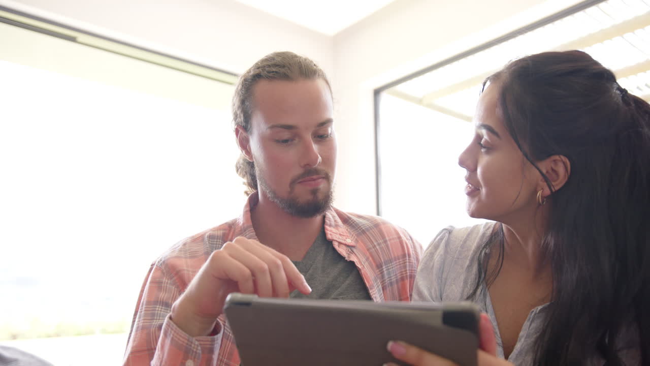 una pareja diversa usa una tableta en un sofá de fondo blanco