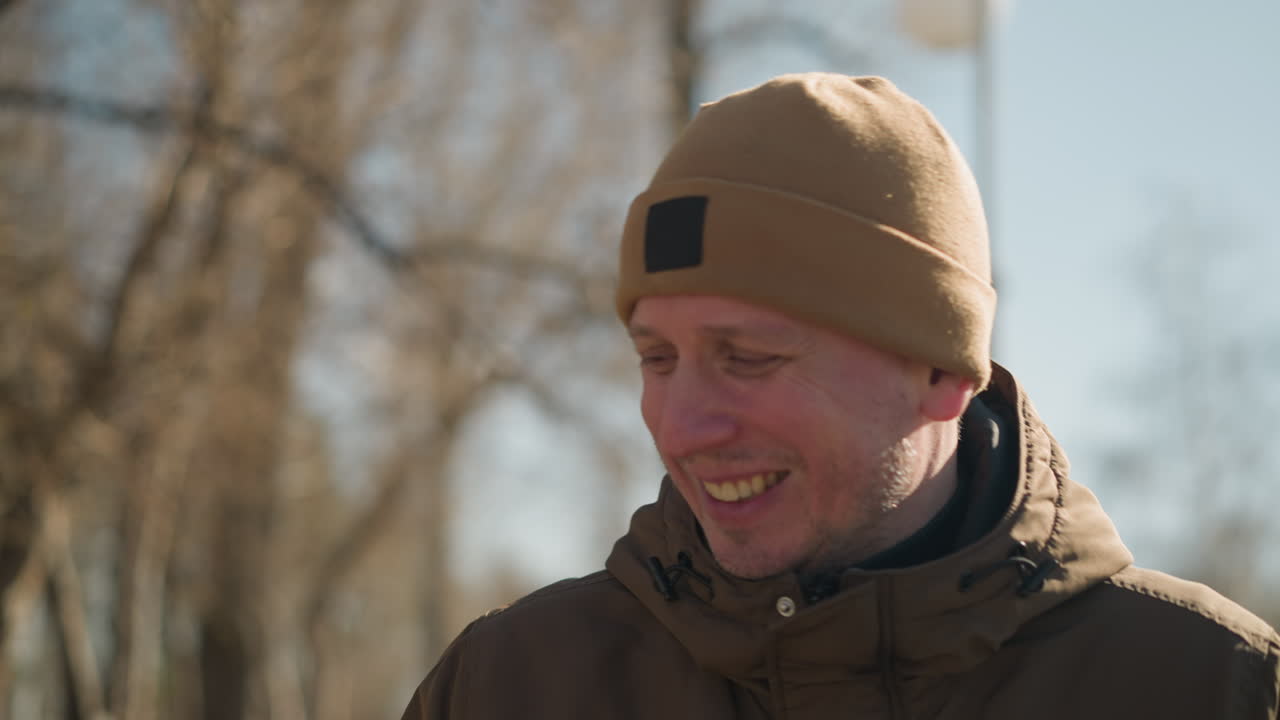 отец и сын держат друг друга за руку, гуляя на улице. ребёнок, одетый в блестящую черную куртку и черную шапочку, смотрит на отца с улыбкой на спине.