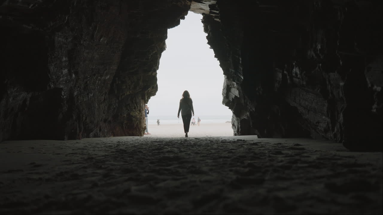 Person Walking Out of a Dark Cave onto a Bright Beach