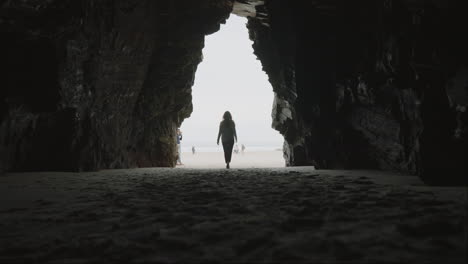 person walking out of a dark cave onto a bright beach