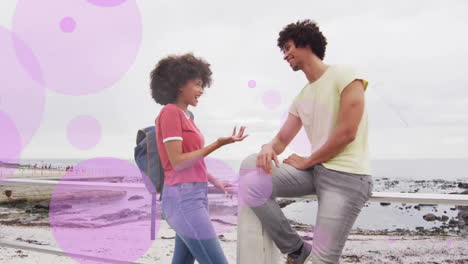 animación de manchas púrpuras sobre una feliz pareja biracial hablando en el paseo marítimo