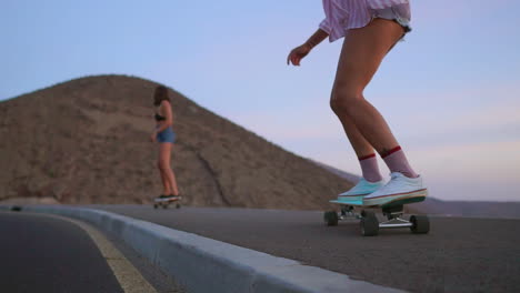 amid the beauty of sunset, two friends wearing shorts engage in slow-motion skateboarding on a road, with mountains and a stunning sky as the backdrop