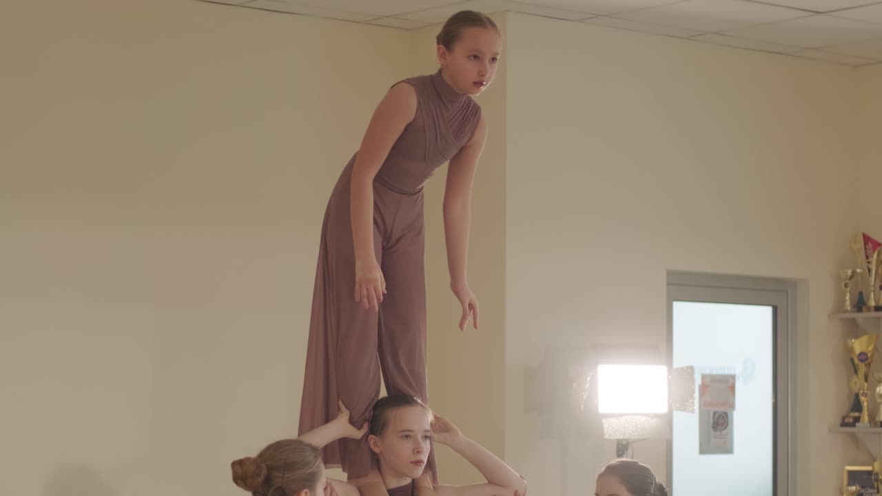 группа молодых студентов балета в черной танцевальной одежде практикует позиции в просторной балетной студии с деревянным полом и настенными решетками. сосредоточенные выражения и синхронизированные движения.