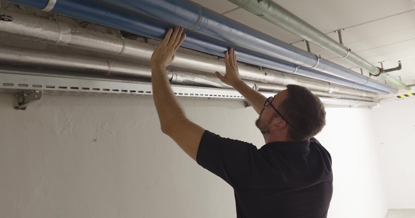 Man inspecting overhead pipes and utility lines, representing maintenance, technical inspection and fire safety.