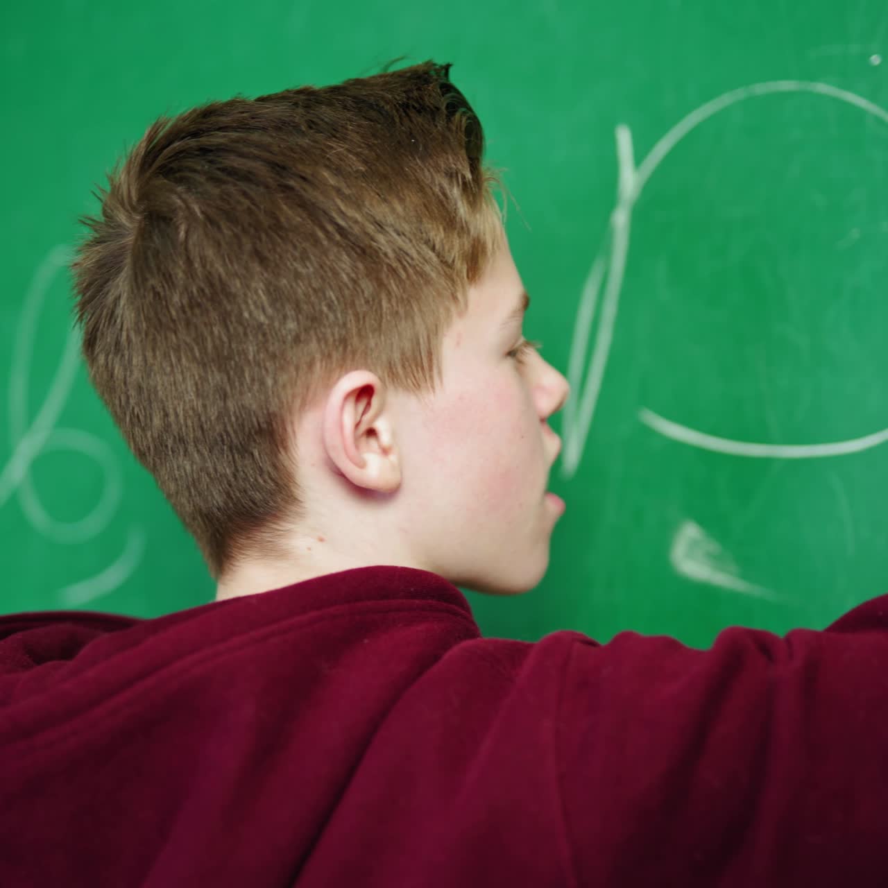 Teenage boy studying at school. Schoolboy standing in the classroom and writes on blackboard with a white chalk. Education concept.