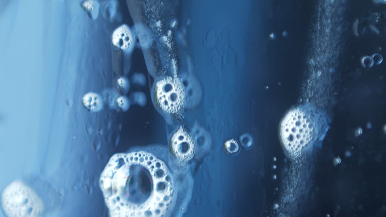 비누 거품의 매크로 사진, 창문 청소 화학, 유리 아래로 흐르는 아름다운 반사.