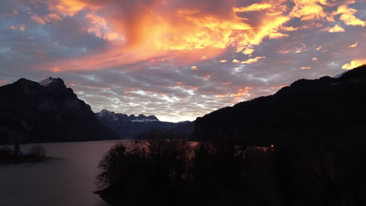 Warm sunset clouds reflecting over a calm alpine lake surrounded by dark mountain silhouettes