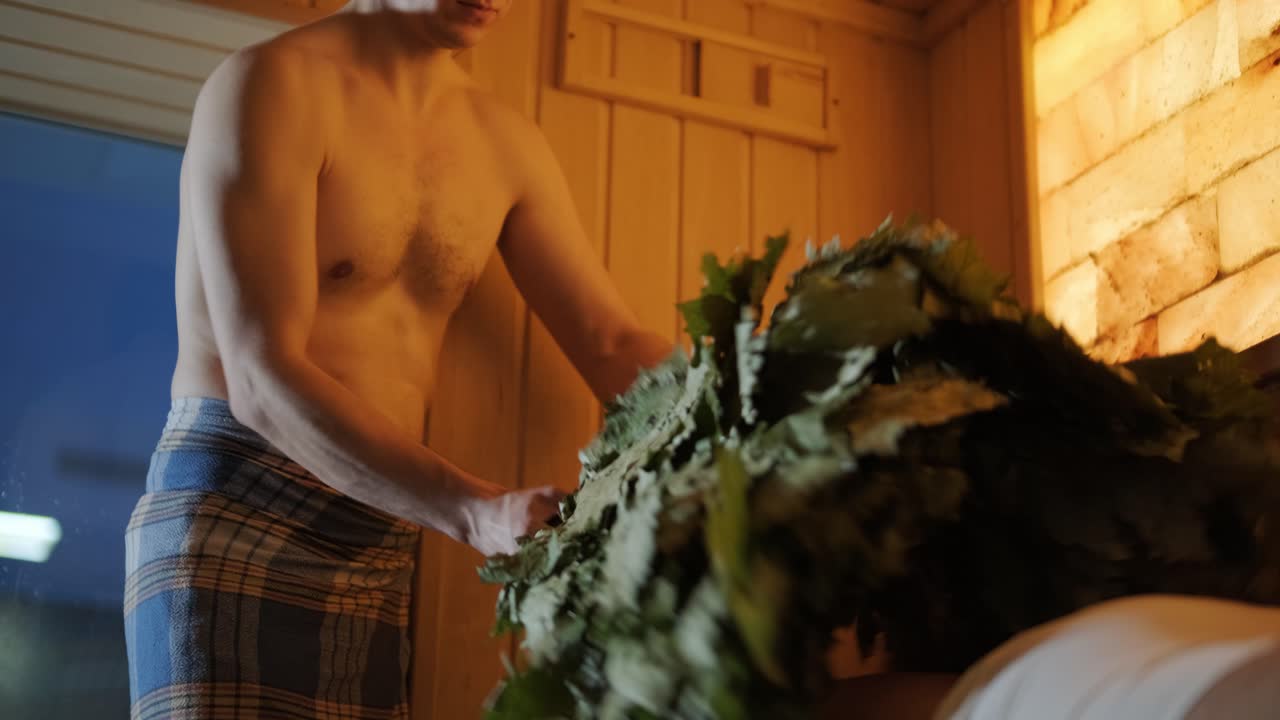 스파에서 나무 벤치에 누워있는 남자와 마사지 마사지하는 오크 자루와 함께 핀 사우나에서 실내에서 전문가와 함께 클라이언트.