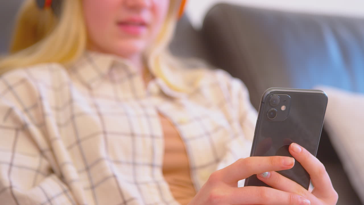 휴대폰에서 콘텐츠를 스트리밍하는 무선 헤드폰을 착용한 소파에 있는 십대 소녀의 클로즈업