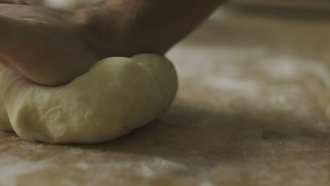 hands kneading dough on wooden kitchen table dusted with flour