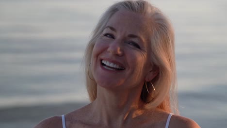 Portrait-of-beautiful-mature-blonde-woman-on-a-beach-looking-at-setting-sun-and-then-looking-at-camera