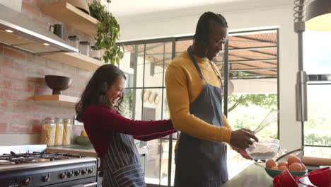 happy diverse couple in aprons baking in sunny kitchen, slow motion