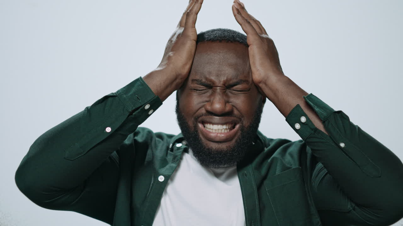 Portrait of exhausted african man holding hands on head at grey background.