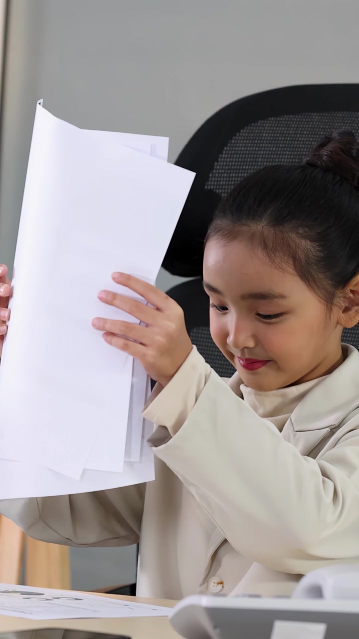 A young girl wearing a professional suit reads and organizes papers at a modern desk.