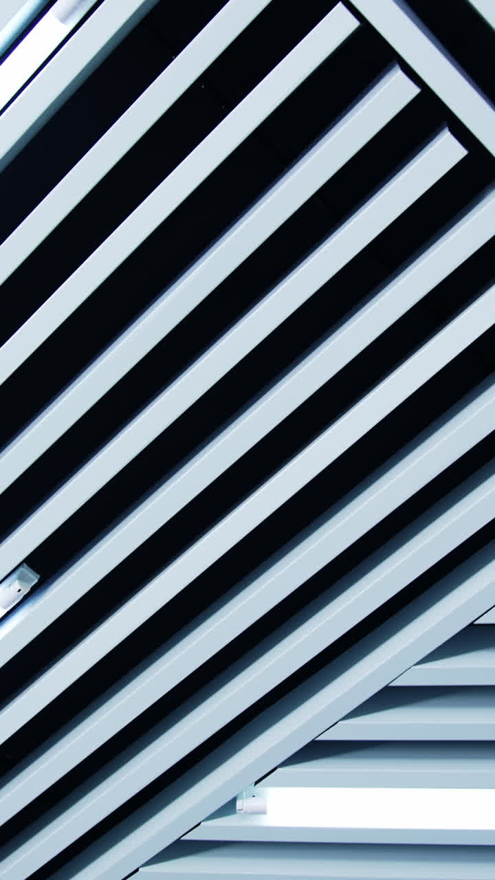 Non-standard decoration of the ceiling with white planks. Long lamps with white light among the ledges. Low angle view. Vertical video