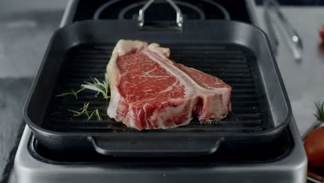 Fresh-steak-preparing-at-griddle-pan.-Closeup-beef-cooking-with-rosemary-at-pan.