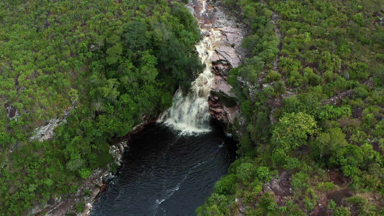 drone aéreo inclinándose hacia abajo de la impresionante cascada del pozo del diablo rodeada de rocas y follaje de la jungla en el hermoso parque nacional chapada diamantina en el noreste de brasil en un día nublado