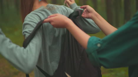 close-up of woman in a red backpack assisting her friend with a black bag, adjusting the straps, the friend, in a blue scarf, turns to look at her friend with a smile, and they began walking