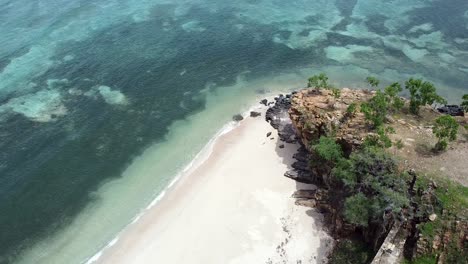 Rising-aerial-drone-of-stunning-white-sandy-beach,-rocky-outcrop-peninsula-in-the-remote-Timor-Leste,-South-East-Asia