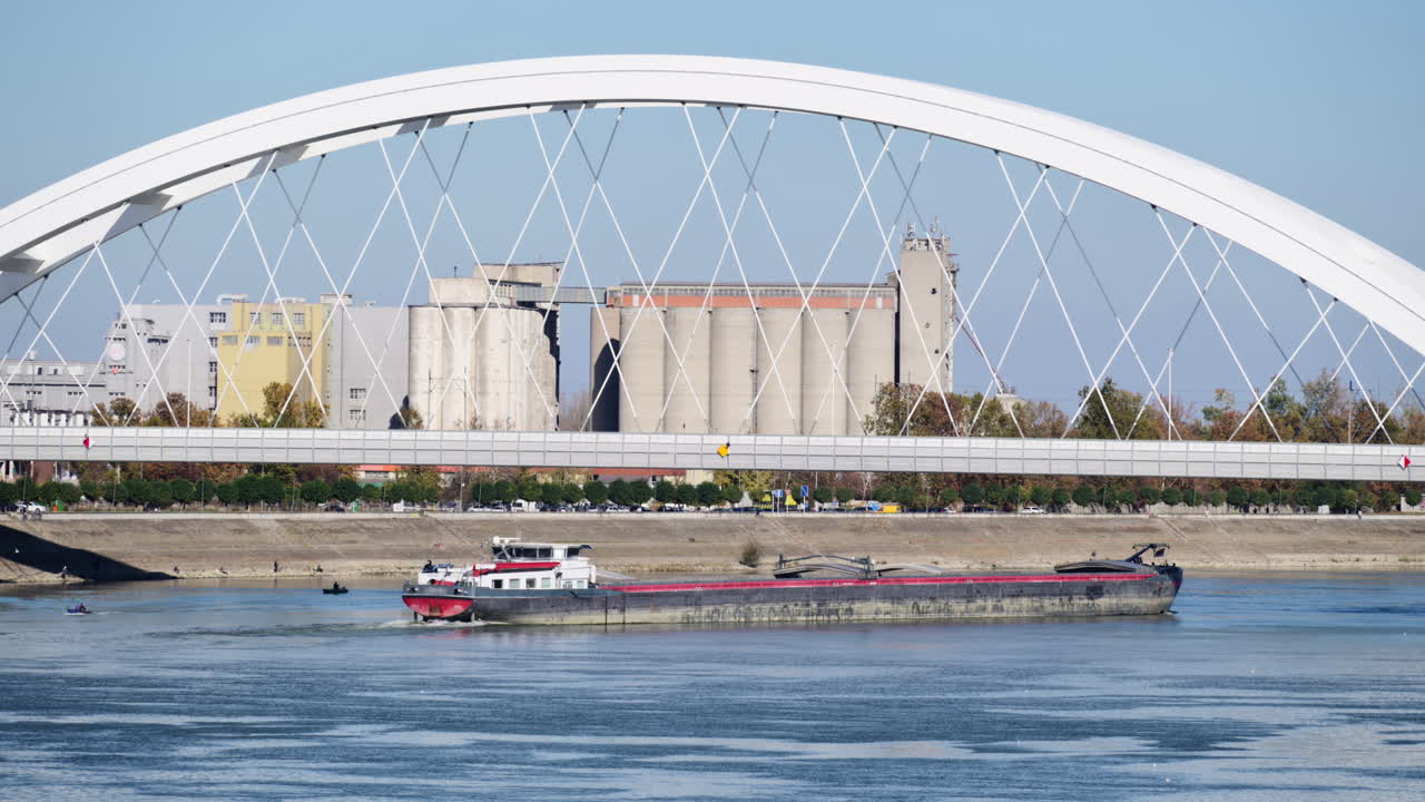 Chiatta da carico in navigazione sul fiume Danubio sotto il ponte Žeželj con impianti industriali sulla riva del fiume. Novi Sad, Serbia