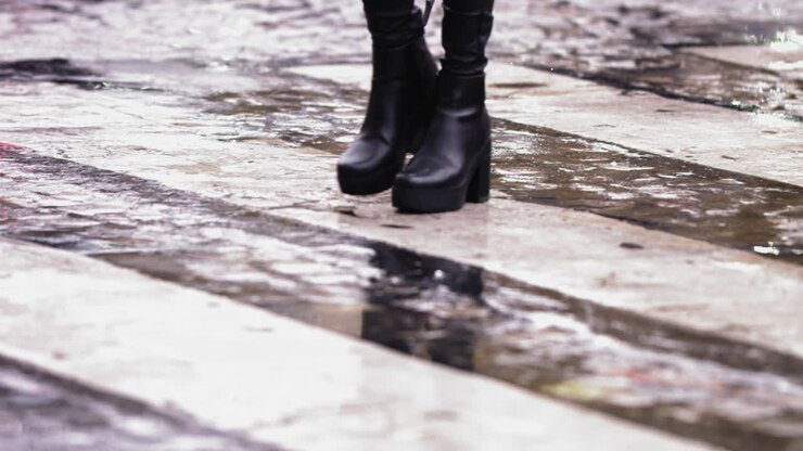 Super slow motion footage of black high heel boots walking across a wet crosswalk in the rain