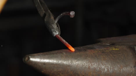 Close-up-of-an-incandescent-piece-of-metal,-hammered-on-the-anvil