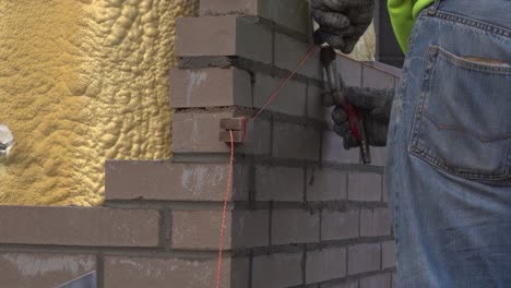 Hombre-Alineando-Ladrillos-Para-Nivelarlos-Con-Una-Cuerda-Durante-La-Construcción-De-Paredes