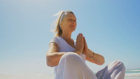 Vista-De-ángulo-Bajo-De-Una-Mujer-Caucásica-Senior-Activa-Realizando-Yoga-En-La-Playa-4k