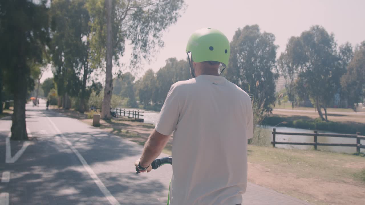 Vista posteriore di un uomo in monopattino elettrico in una giornata di sole al Parco Yarkon, Tel Aviv, Israele