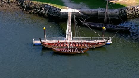 a person on the jetty gets on some viking exhibition boats on the ulla river, sunny summer afternoon, overhead drone shooting