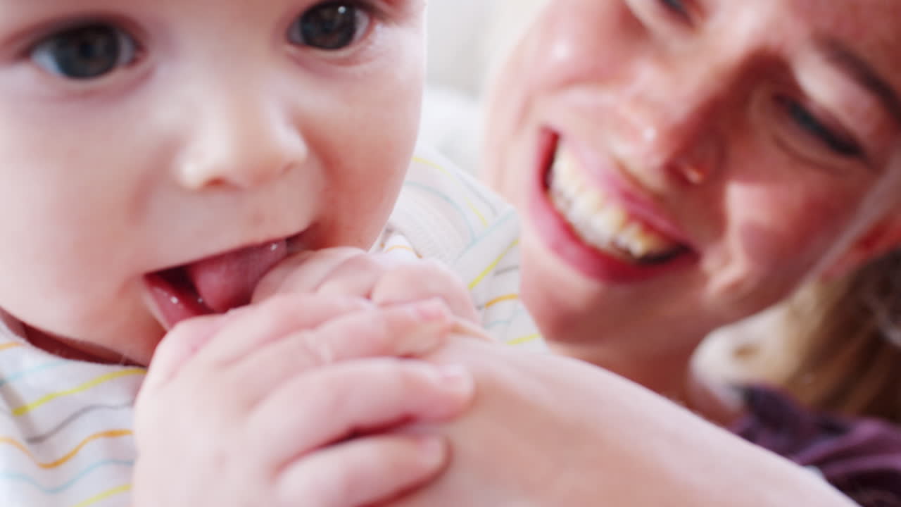Mother holds teething baby, chewing father&rsquo;s hand, close up
