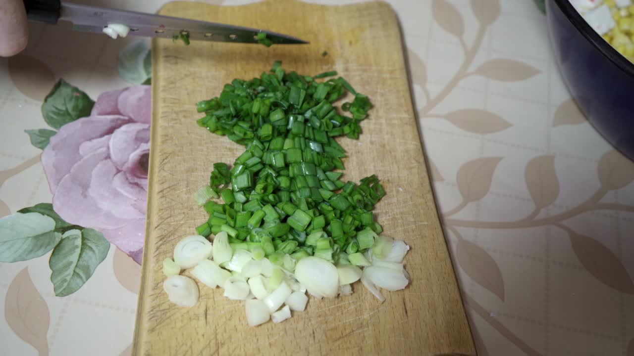 Green onions are cut on a wooden board and poured into a bowl of crab sticks