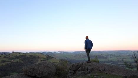 un hombre en un mirador bajo el sol de la mañana temprano con nubes rodando a través del paisaje en el país alto de victoria