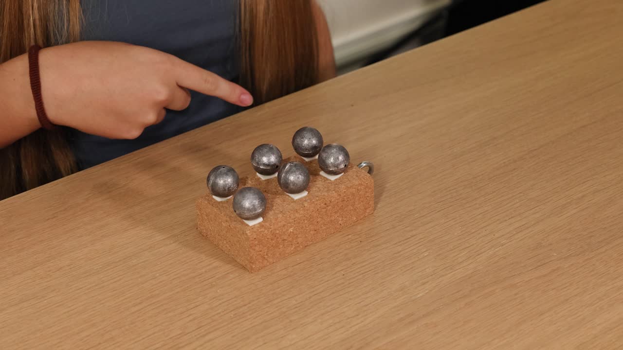 A girl manipulates metal balls on a cork block, exploring balance and movement. Neutral lighting and steady camera focus on hands