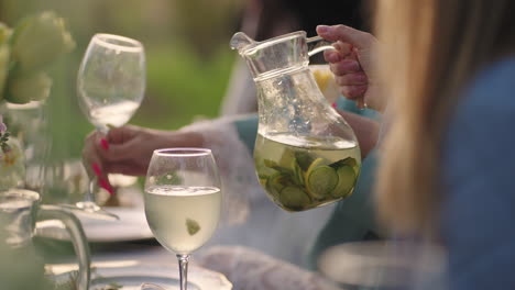 woman is pouring cold lemonade into glasses open-air party in garden in nature catering and beverage