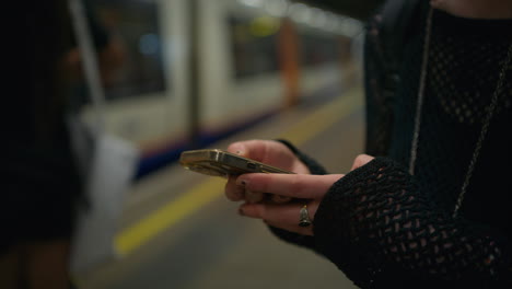 close up shot of alternative style woman using mobile phone on platform of london underground train station in real time