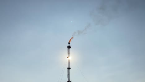 Telephoto-shot-of-Gas-Flare-burning-against-sun,-handheld,-industry,-day