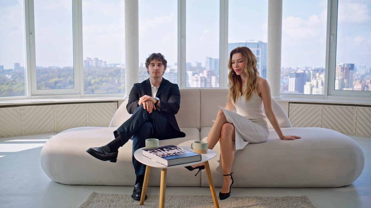 Coppia elegante seduta sul divano di un attico di lusso. Uomo e donna che si rilassano in una casa con vista sulla città.