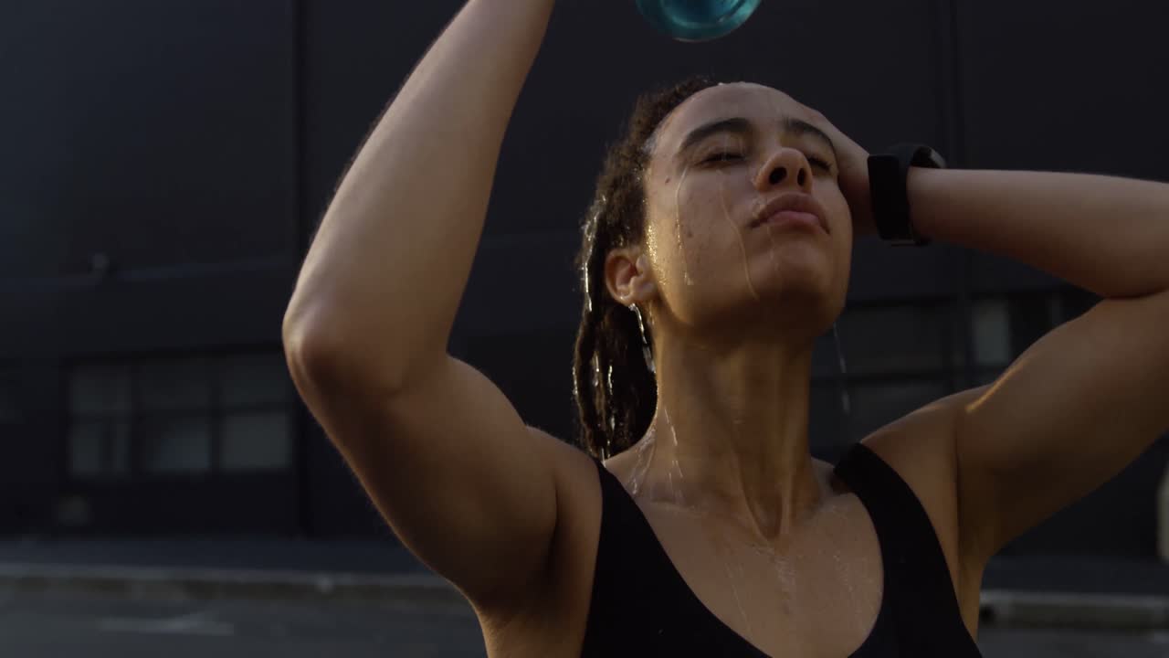 vista frontal de una joven mujer afroamericana vertiendo agua en su cabeza en la ciudad 4k