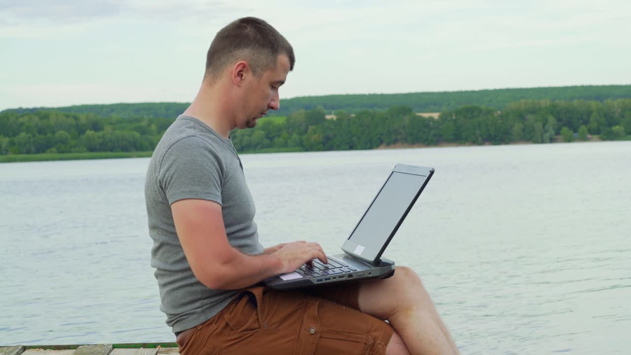 Man is typing on a laptop and beautiful nature around him inspires to work. Handsome male working during the rest. Close-up