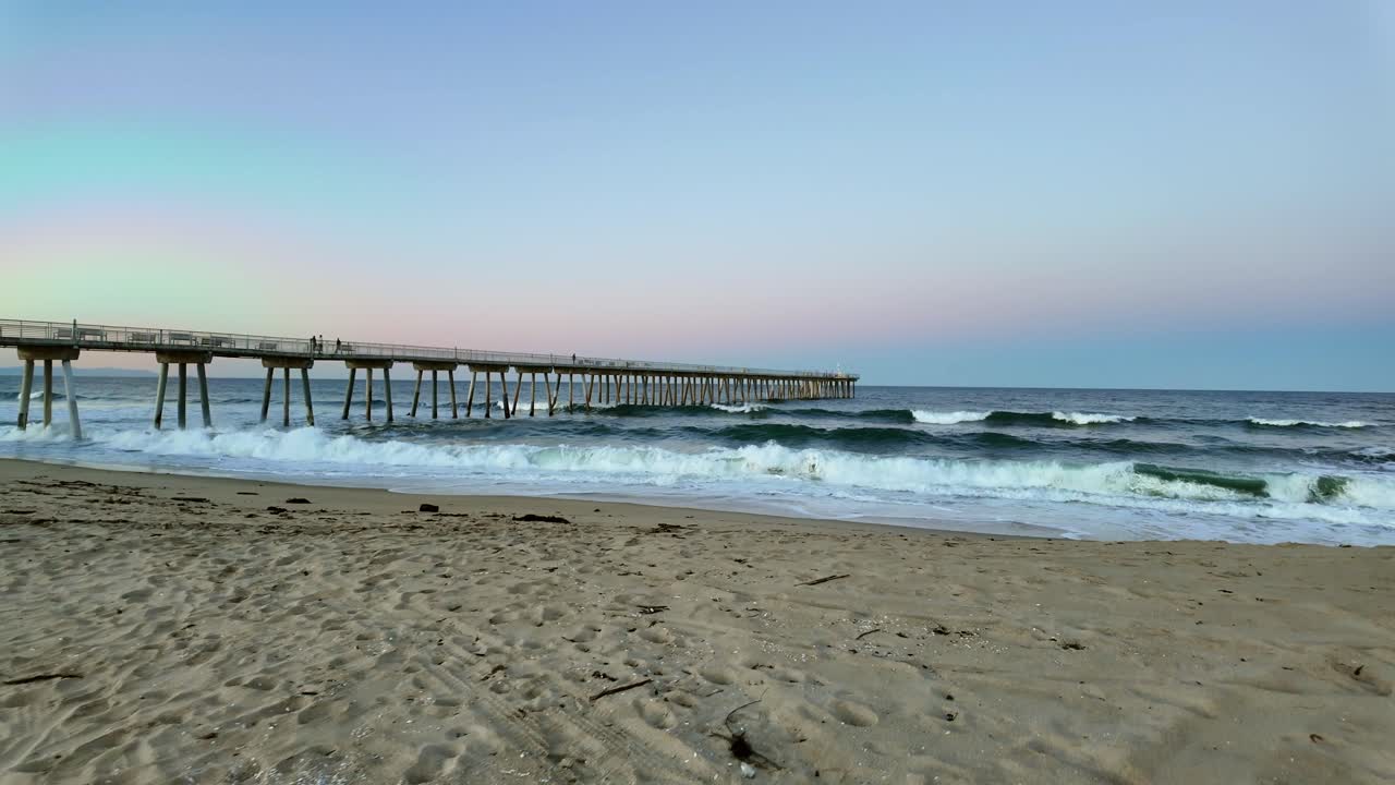 el amanecer se rompe sobre la playa de hermosa con las olas golpeando suavemente y un muelle sereno en el fondo, toma amplia