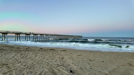 El-Amanecer-Amanece-En-La-Playa-Hermosa-Con-Olas-Rompiendo-Suavemente-Y-Un-Muelle-Sereno-Al-Fondo,-Plano-General