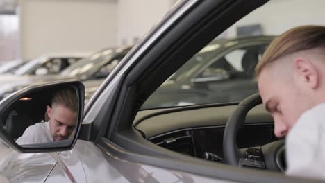 happy beard long haired male customer in vehicle showroom, male person buying transport, auto dealer business. man looking at the new car. consumer in car dealership. business man choosing a car.