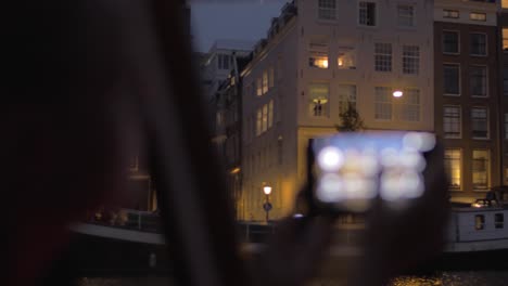 Woman-traveling-by-boat-in-night-Amsterdam-and-taking-photos