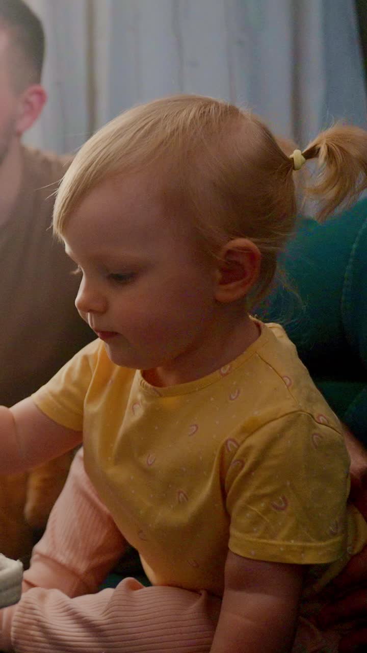 A Close-Up Portrait of a Curious Child with Light Blond Hair and Bright Blue Eyes, Engaged in Play While Indoors with a Soft Surrounding, Capturing a Moment of Joy and Innocence